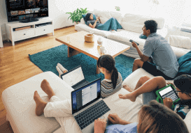A Family together in a room, securely looking at individual screens while watching TV