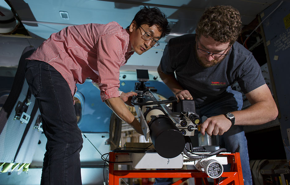 Deux experts travaillant sur un récepteur de distribution de clés quantiques, un appareil de la taille d’un télescope monté sur une plateforme basse.